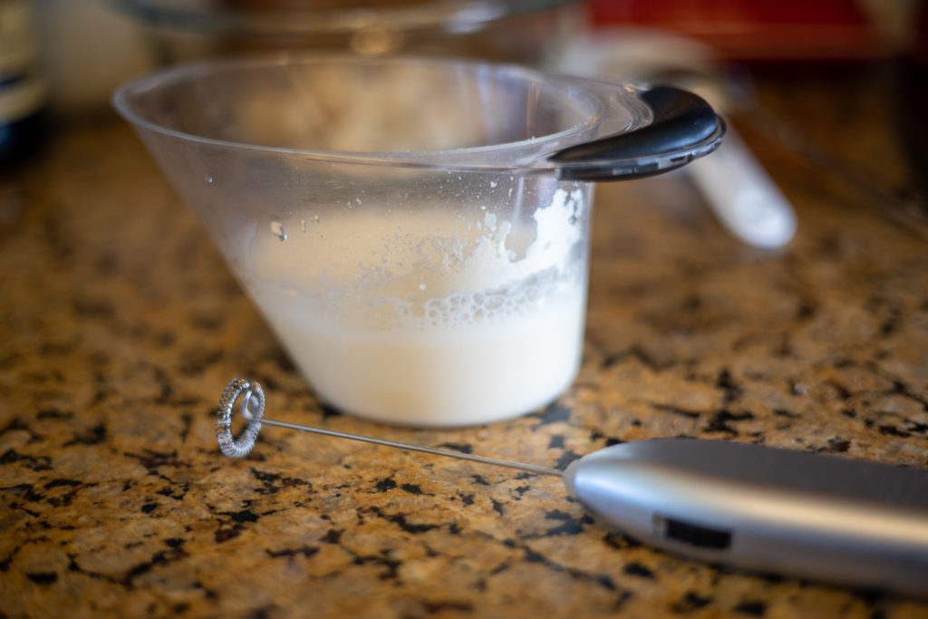 a milk frother and powdered buttermilk mixed into water in a measuring cup