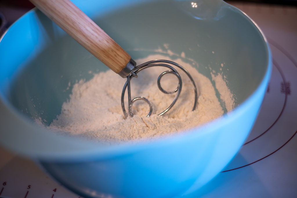 a dough whisk sitting in a blue bowl of dry ingredients