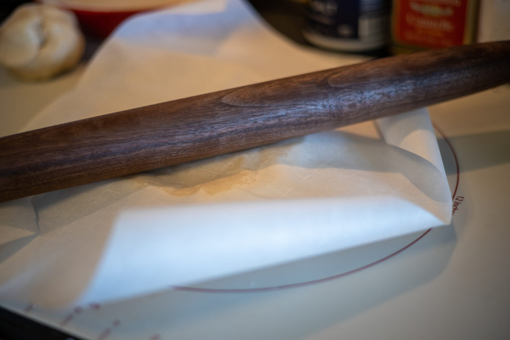 dough being rolled under wax paper with a wooden rolling pin