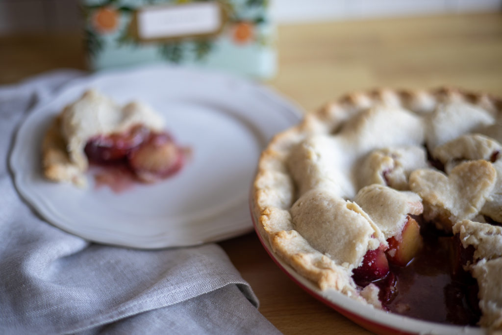 a piece of plum pie on a plate behind a whole pie