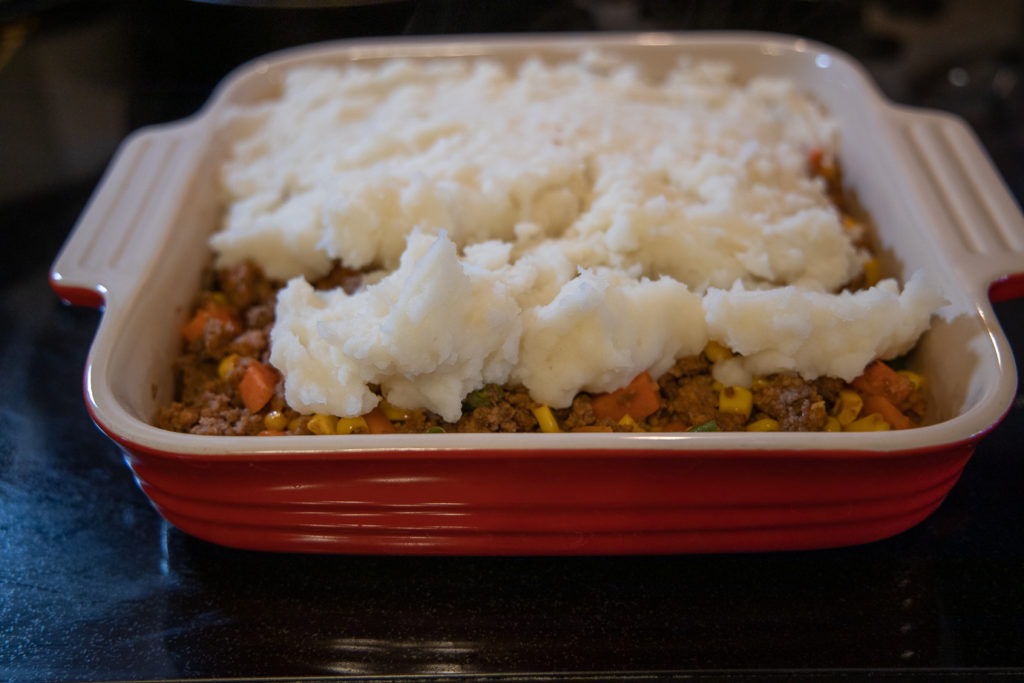 the shepherd's pie filling halfway covered with mashed potatoes