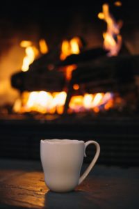 a white mug on a hearth in front of a lit fire